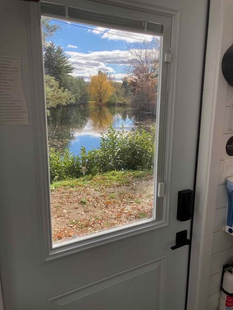Scenic view from tiny home's window overlooking a peaceful lake and colorful autumn trees.