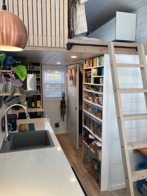 Compact tiny house kitchen with loft storage and organized shelves for small space living.