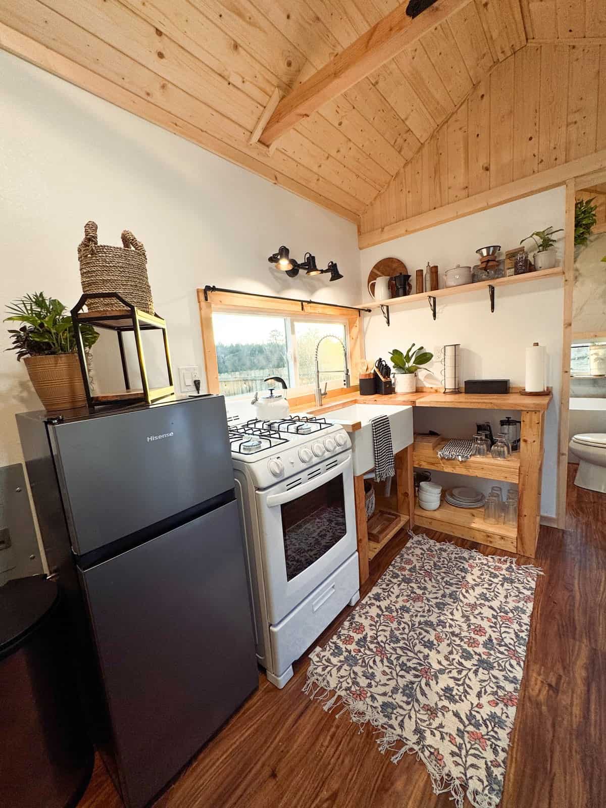 Surya tiny house kitchen with a full-size range and oven, a refrigerator, a butcher-block counter, a farmhouse sink, and open shelving under a vaulted pine ceiling