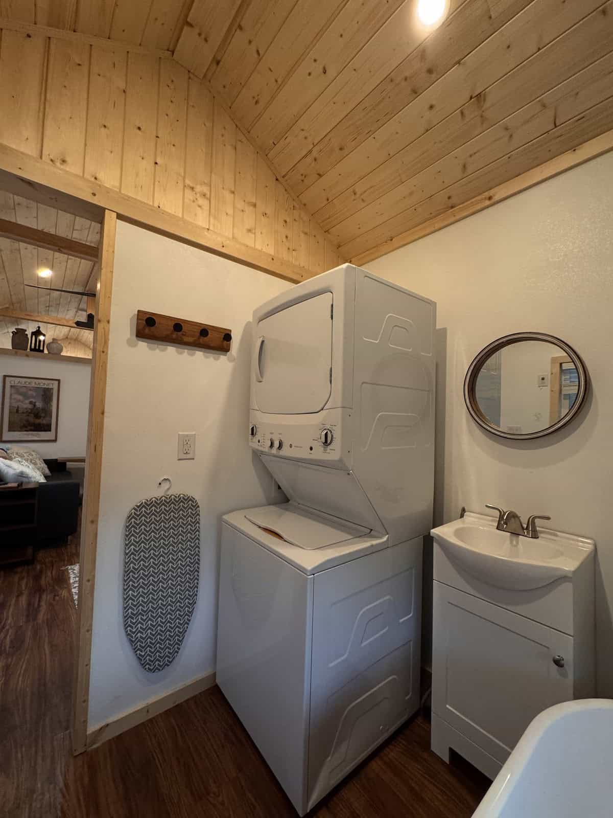 Stackable washer and dryer beside a vanity in the Surya tiny house, with the freestanding tub alongside