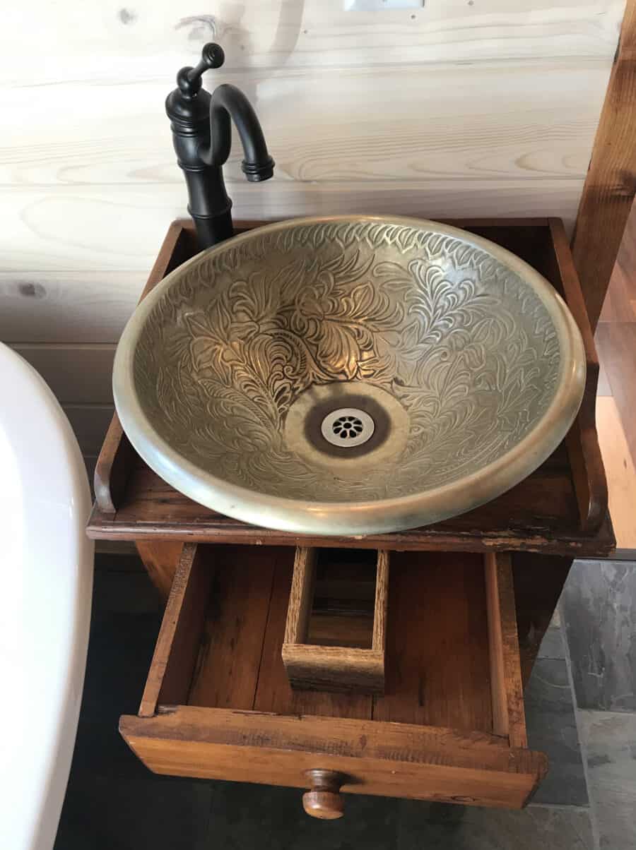 Rustic brass sink with black faucet in tiny house interior.