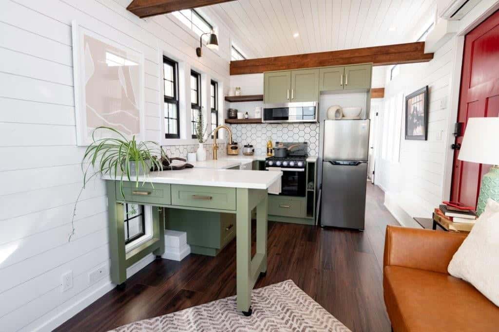 Open kitchen and living area inside the Daphne with sage green cabinets, exposed wood beams and white shiplap