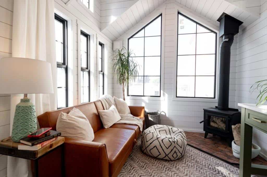 Living room in the Daphne with a leather sofa, cathedral window, brick hearth and black wood stove
