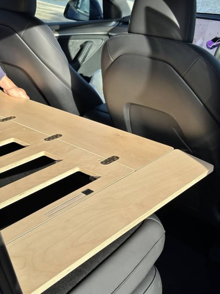 Tesla vehicle interior with a custom wooden camping platform for small space travel.