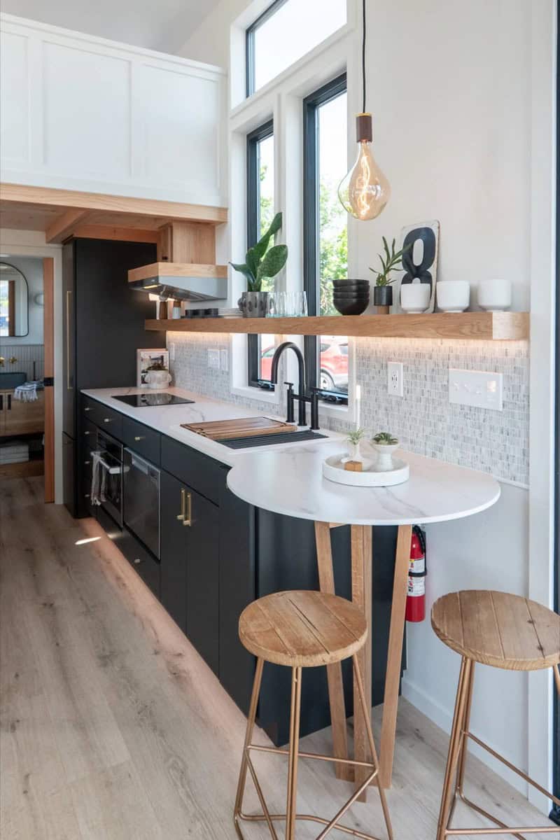 Terra Urban tiny house kitchen with black cabinets, marble counters, induction cooktop and floating wood shelf