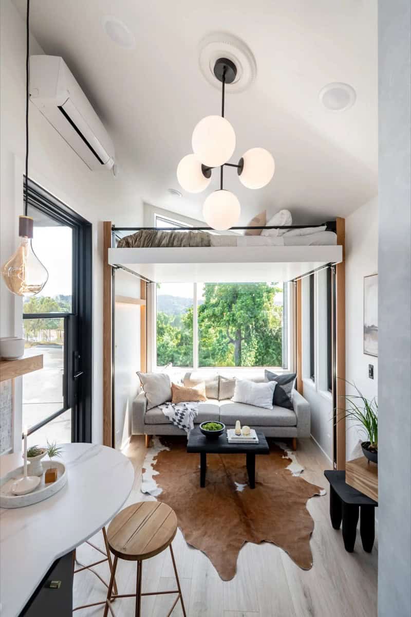 Terra Urban tiny house living room with grey sofa, large windows, vaulted ceiling and globe chandelier