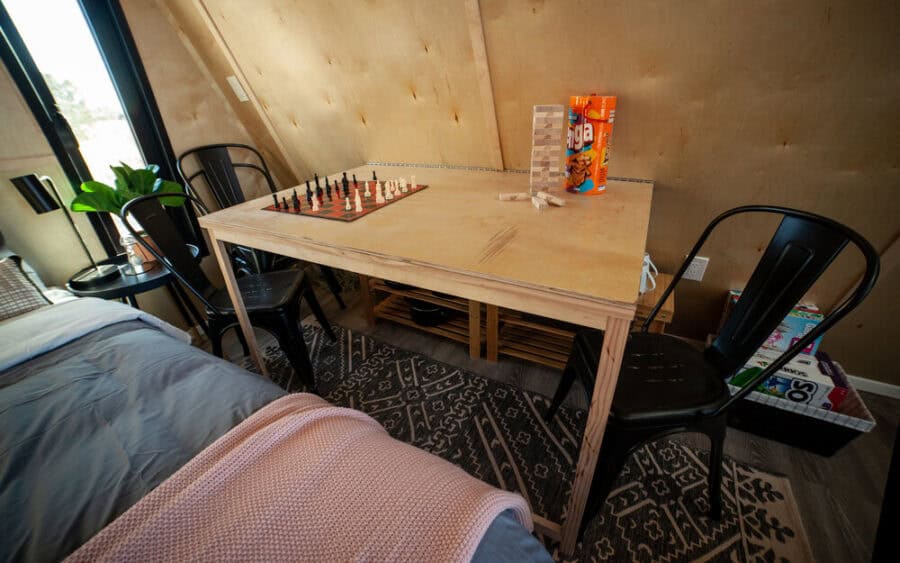 Cozy tiny house interior featuring a wooden chess table and black chairs near a window.