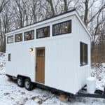 Compact tiny house on wheels with large windows and modern design.