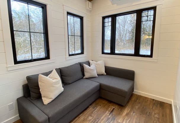 Modern tiny house interior with large windows and a gray sectional sofa.