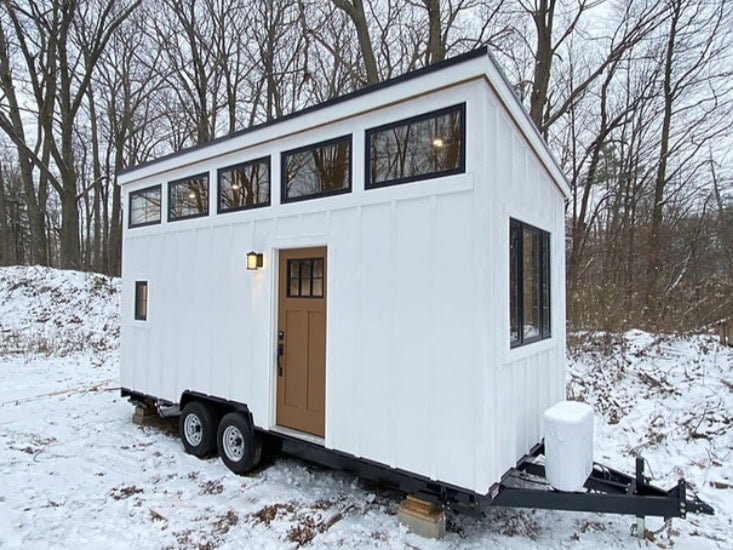Compact tiny house on wheels with large windows and modern design.