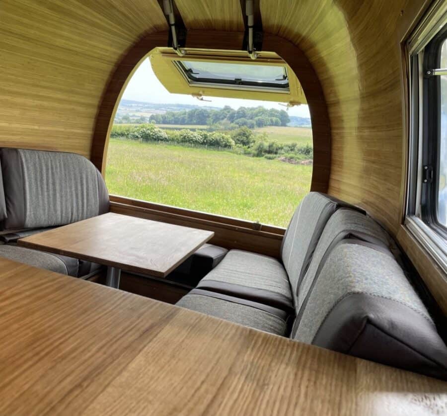 Cozy tiny house interior featuring curved wooden walls, a large window, and comfortable seating for.