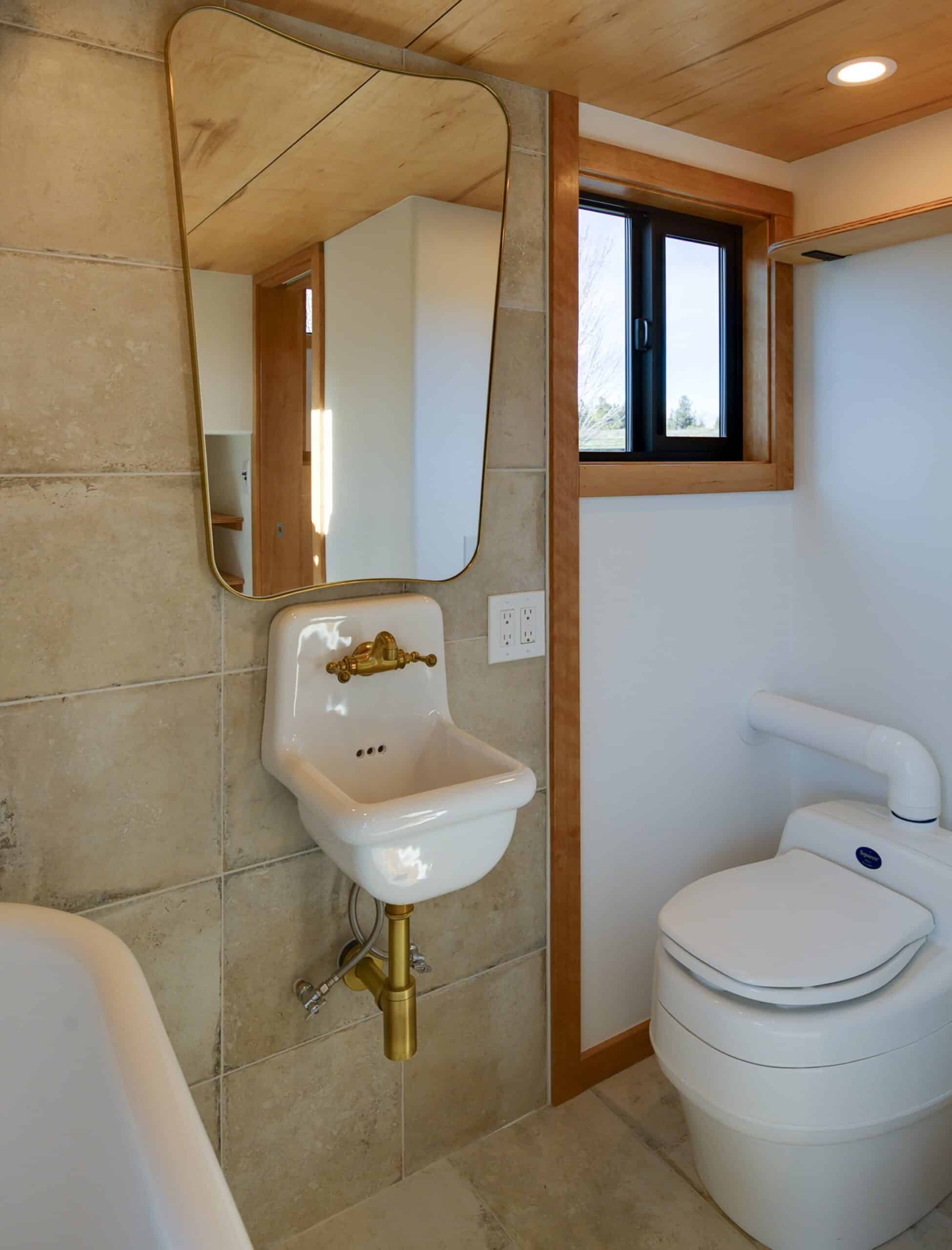 The Black Butte bathroom with a vintage wall-mounted sink, brass fixtures, an asymmetric mirror, and a composting toilet