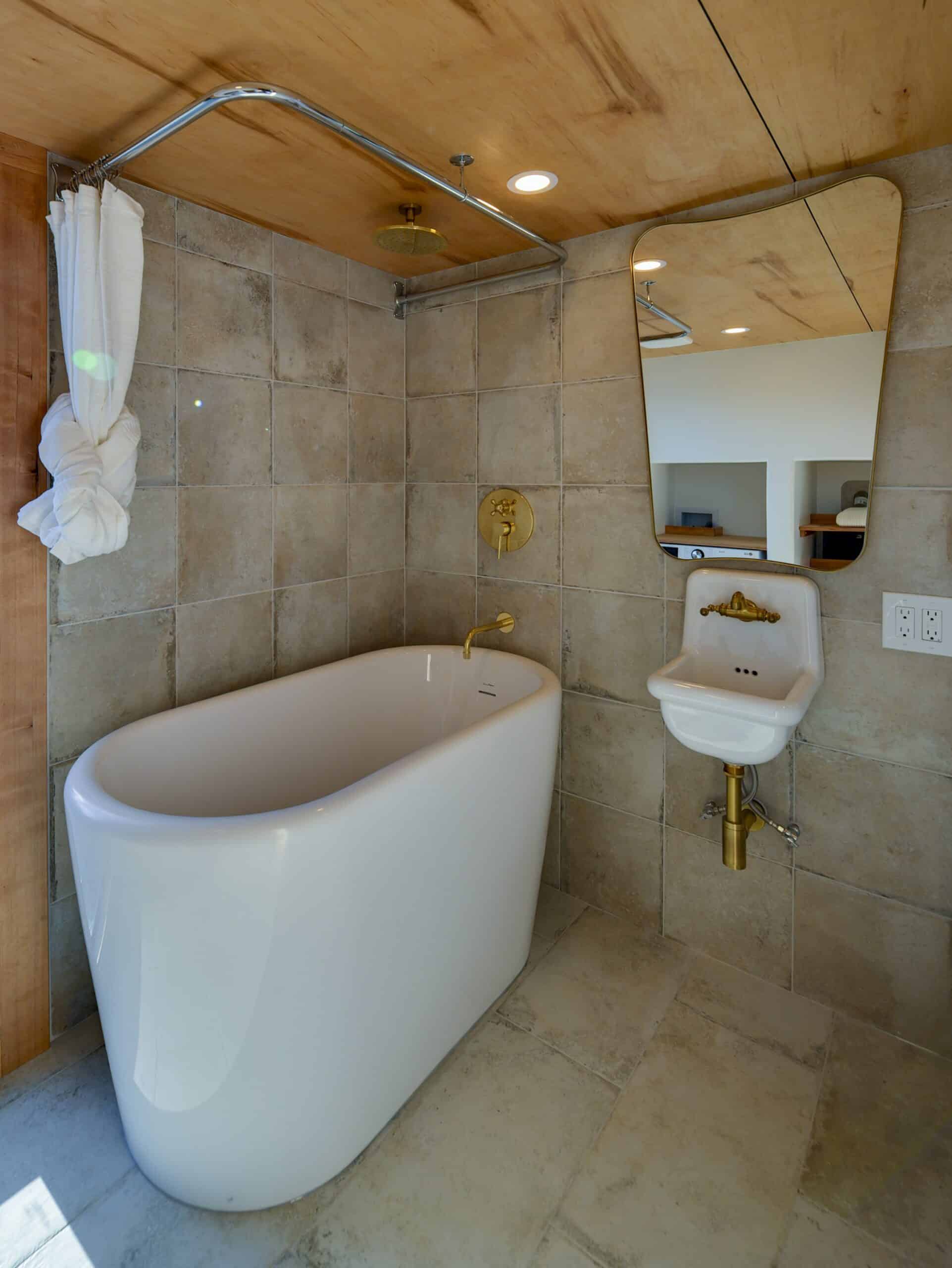 The Black Butte bathroom with a deep freestanding soaking tub, tiled walls, and a brass rainfall shower head