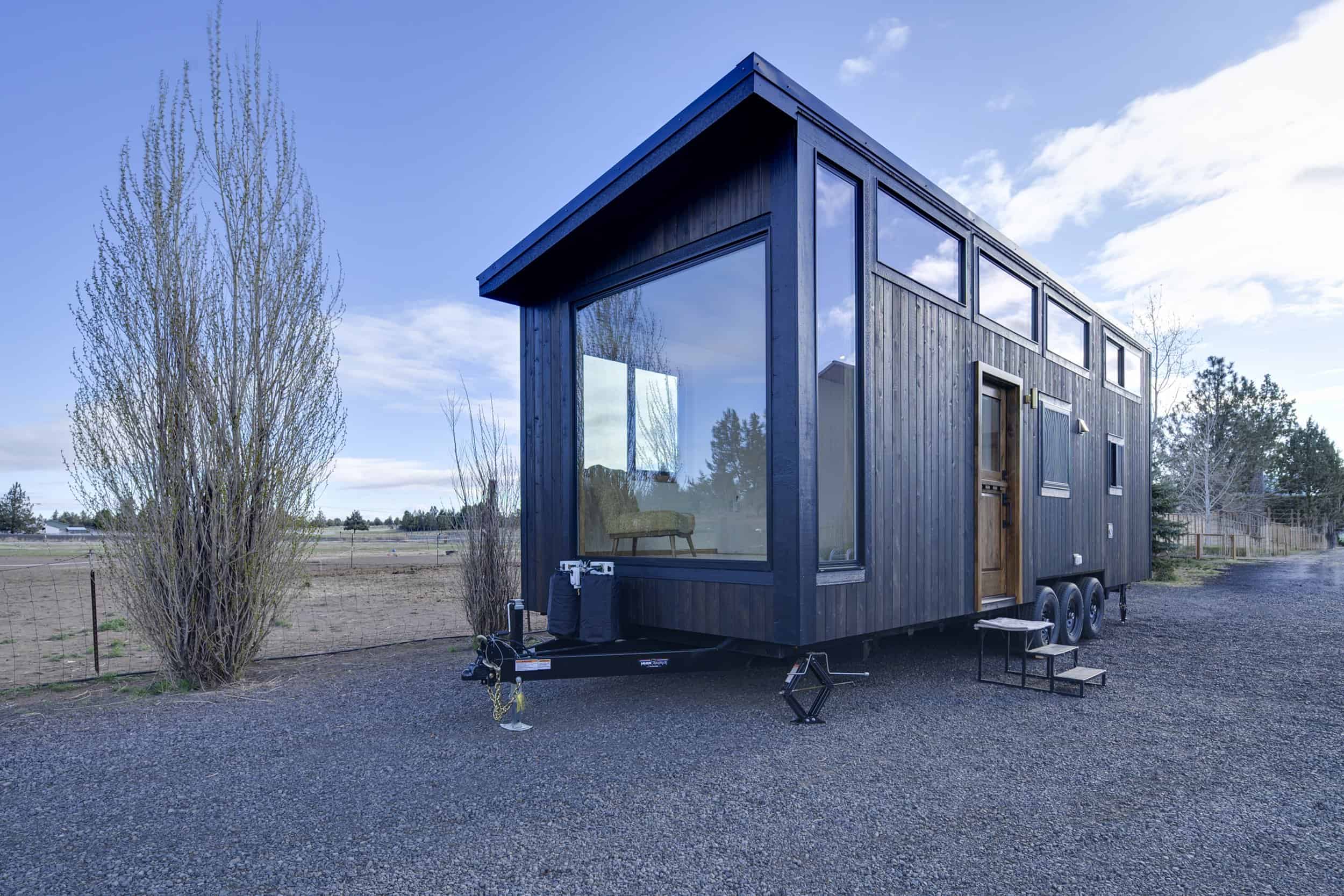 The Black Butte tiny house by Spindrift Homes with dark charred wood siding, a shed roof, and a massive picture window on a triple-axle trailer