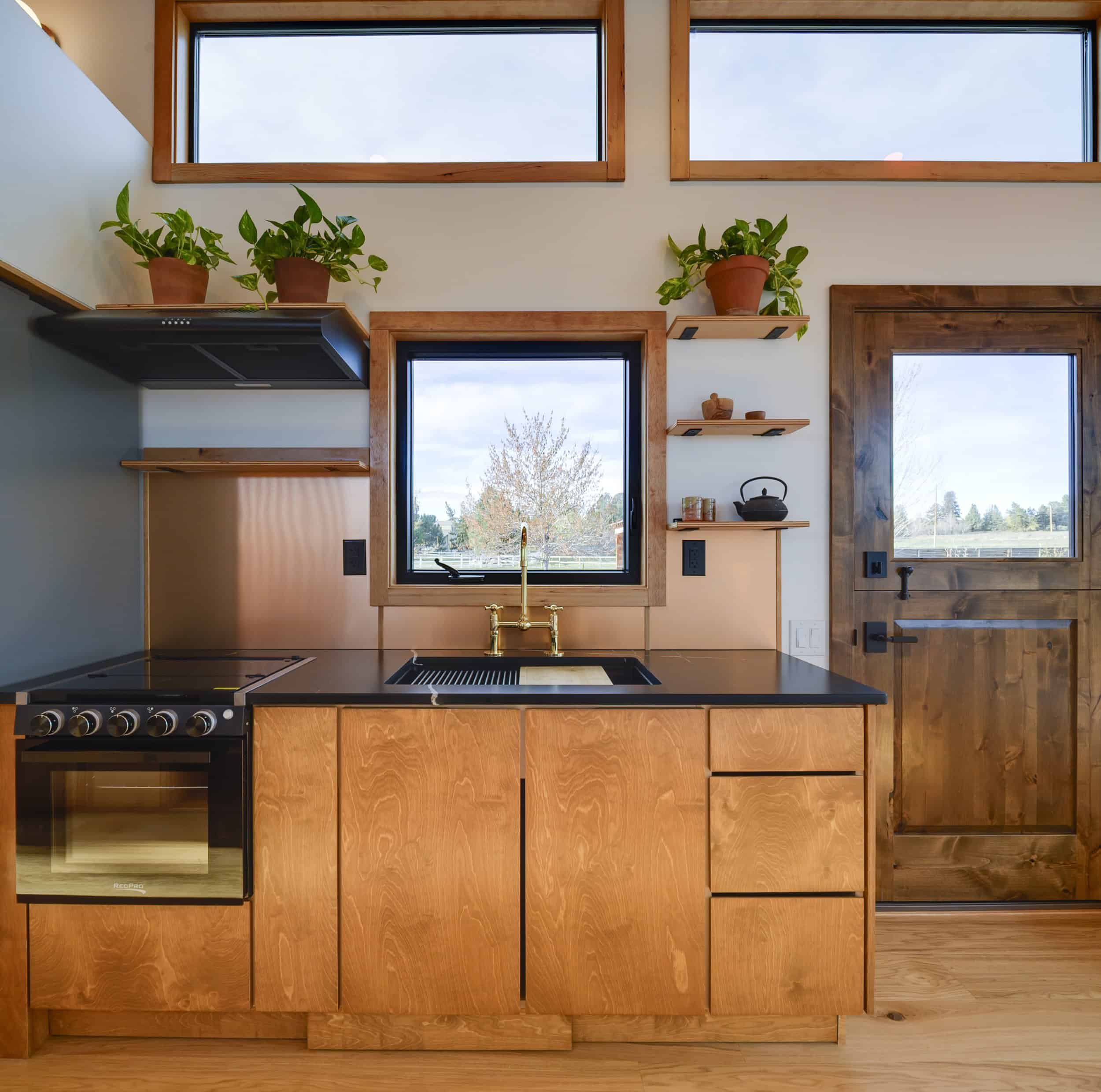 The Black Butte kitchen with Baltic birch cabinetry, black stone counters, a stainless gas range, and a brass faucet