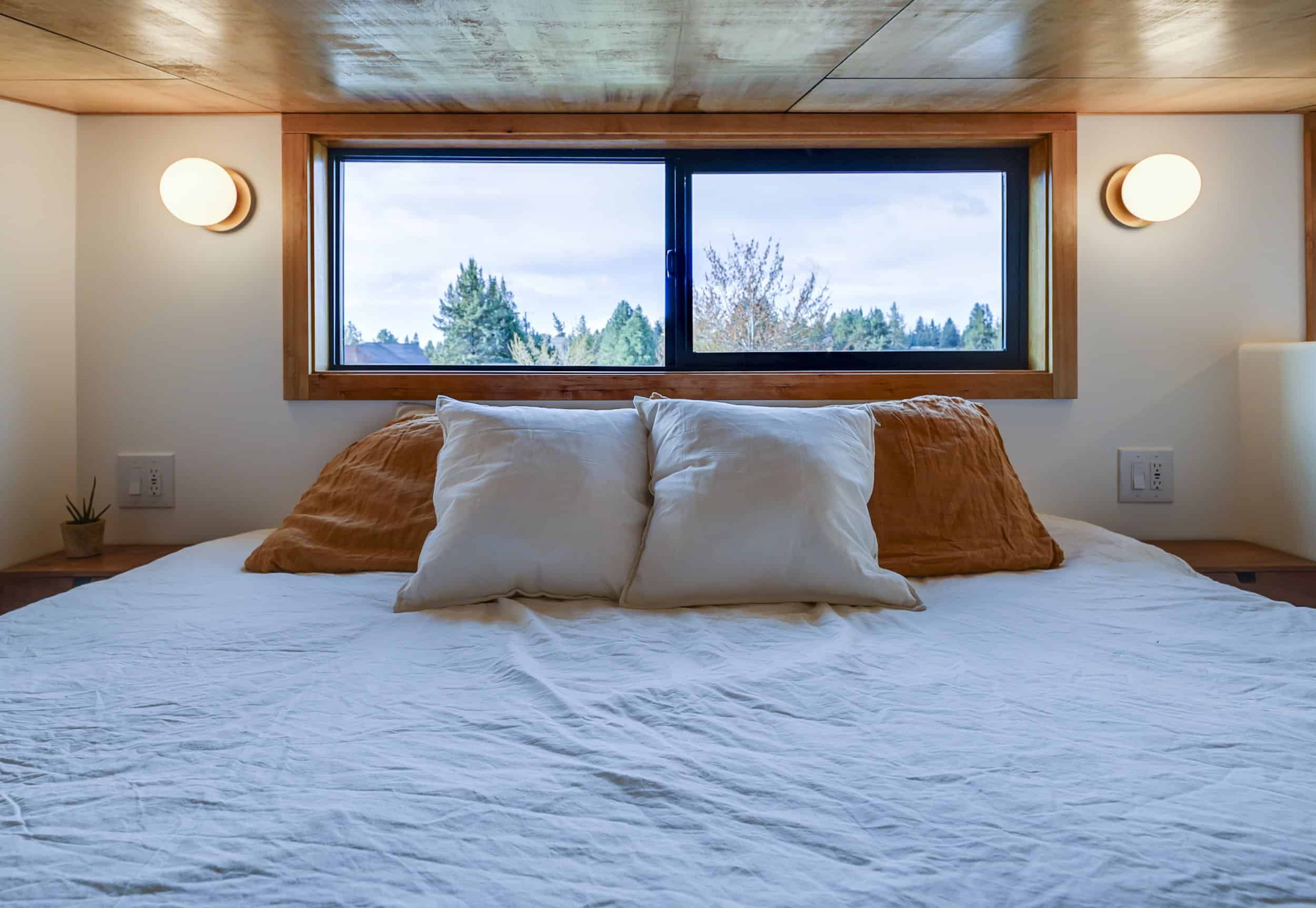 The Black Butte loft bed beneath a wide wood-framed window with round sconces and nightstands