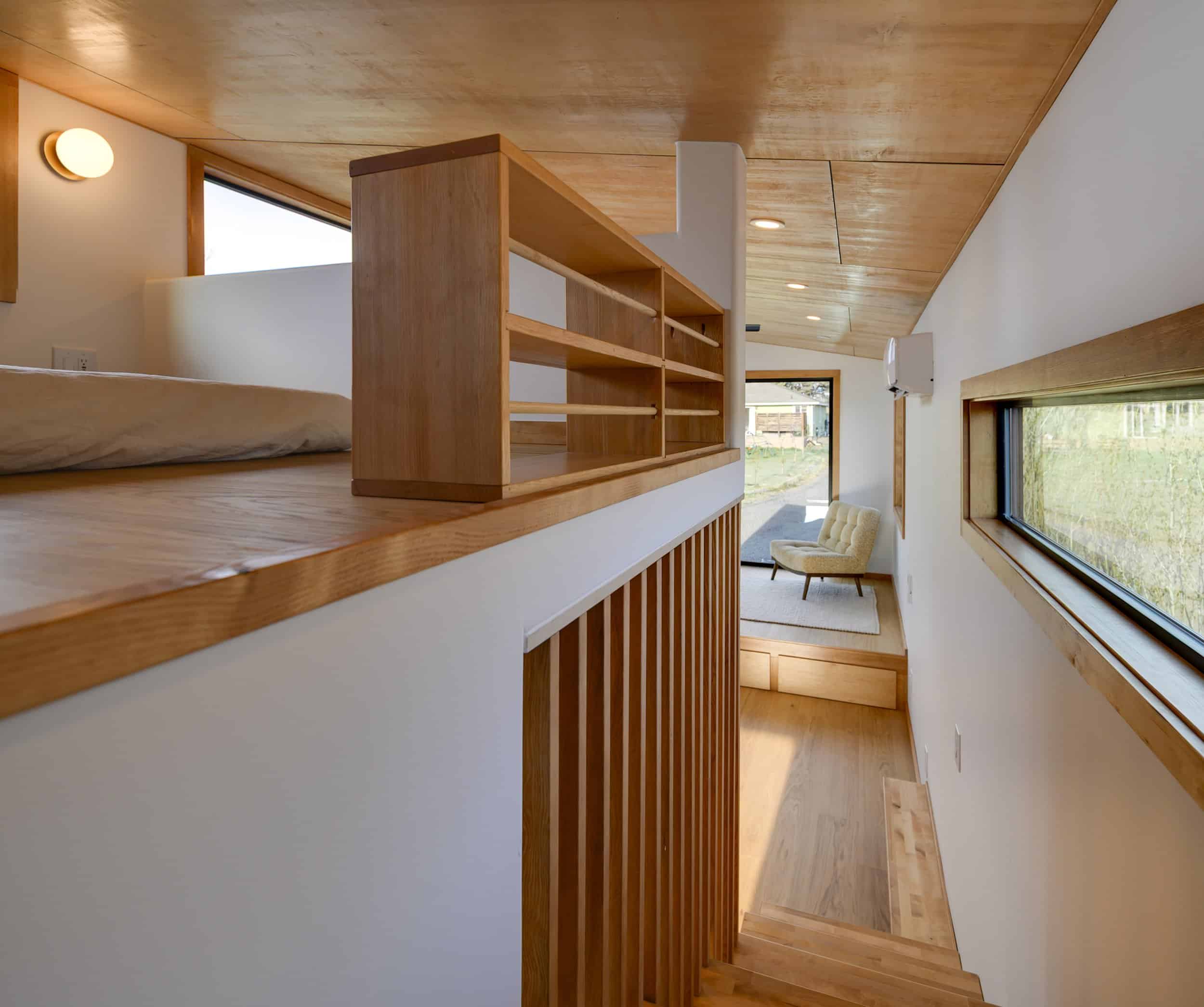 The Black Butte loft bedroom with a built-in oak shelf overlooking the raised platform living room and picture window below