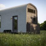 Moody-style 18-ft tiny house on wheels with curved roof in a grassy field.
