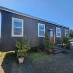 Compact tiny house on wheels with modern black exterior and red door, surrounded by potted plants, s.