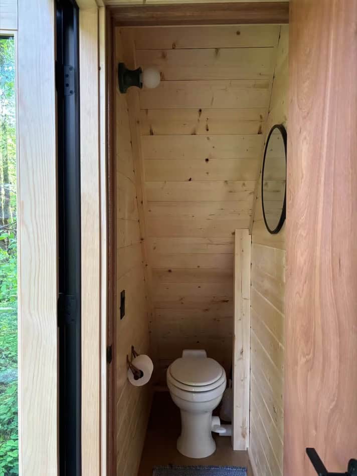 Interior view of a compact tiny house bathroom with wooden walls and a small mirror.