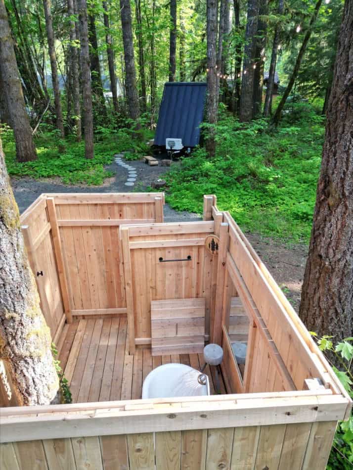 Tiny house outdoor shower and deck in lush forest setting.