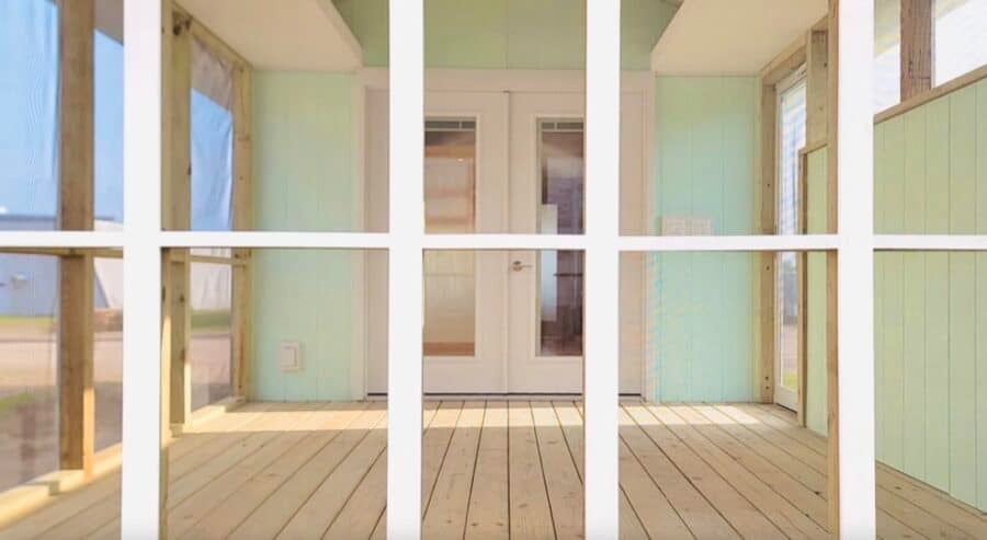 View of a cozy tiny house porch with wooden flooring and large windows.