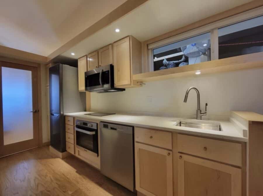 Compact tiny house kitchen with modern appliances and natural wood cabinets.