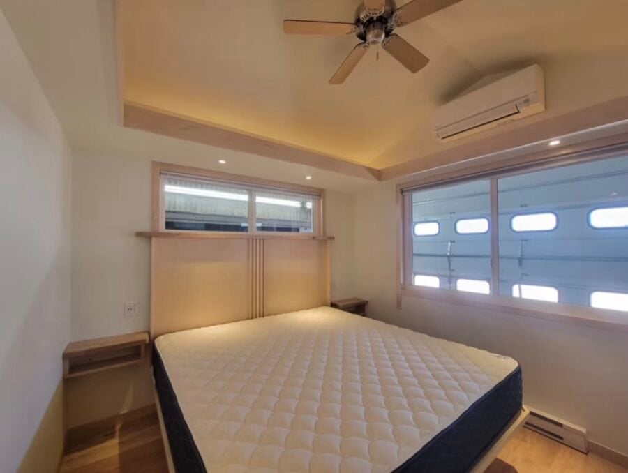 Modern tiny house bedroom with minimalist decor, ceiling fan, and large windows for natural light.