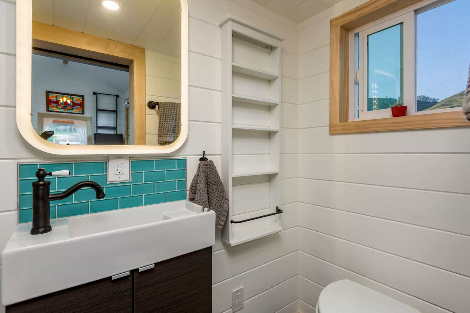 The Joshua Tree bathroom with a farmhouse sink, backlit vanity mirror, teal tile, and recessed wall shelving