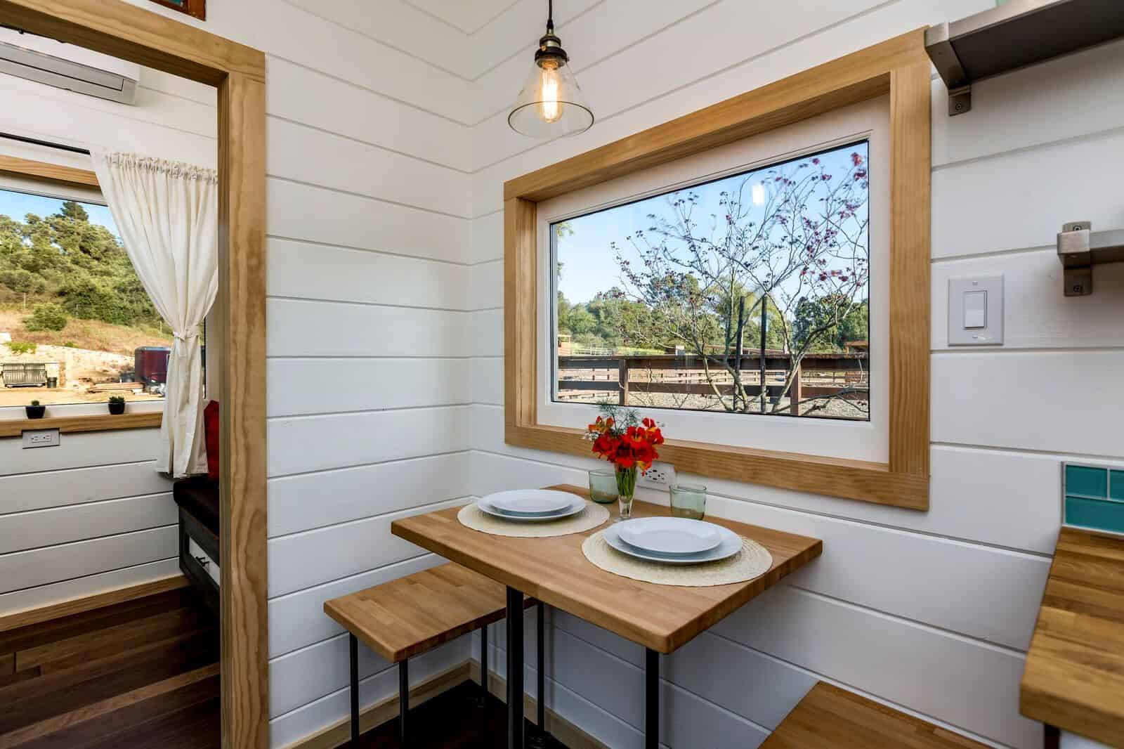 A wood dining nook with two stools beneath a large picture window in the Joshua Tree tiny house