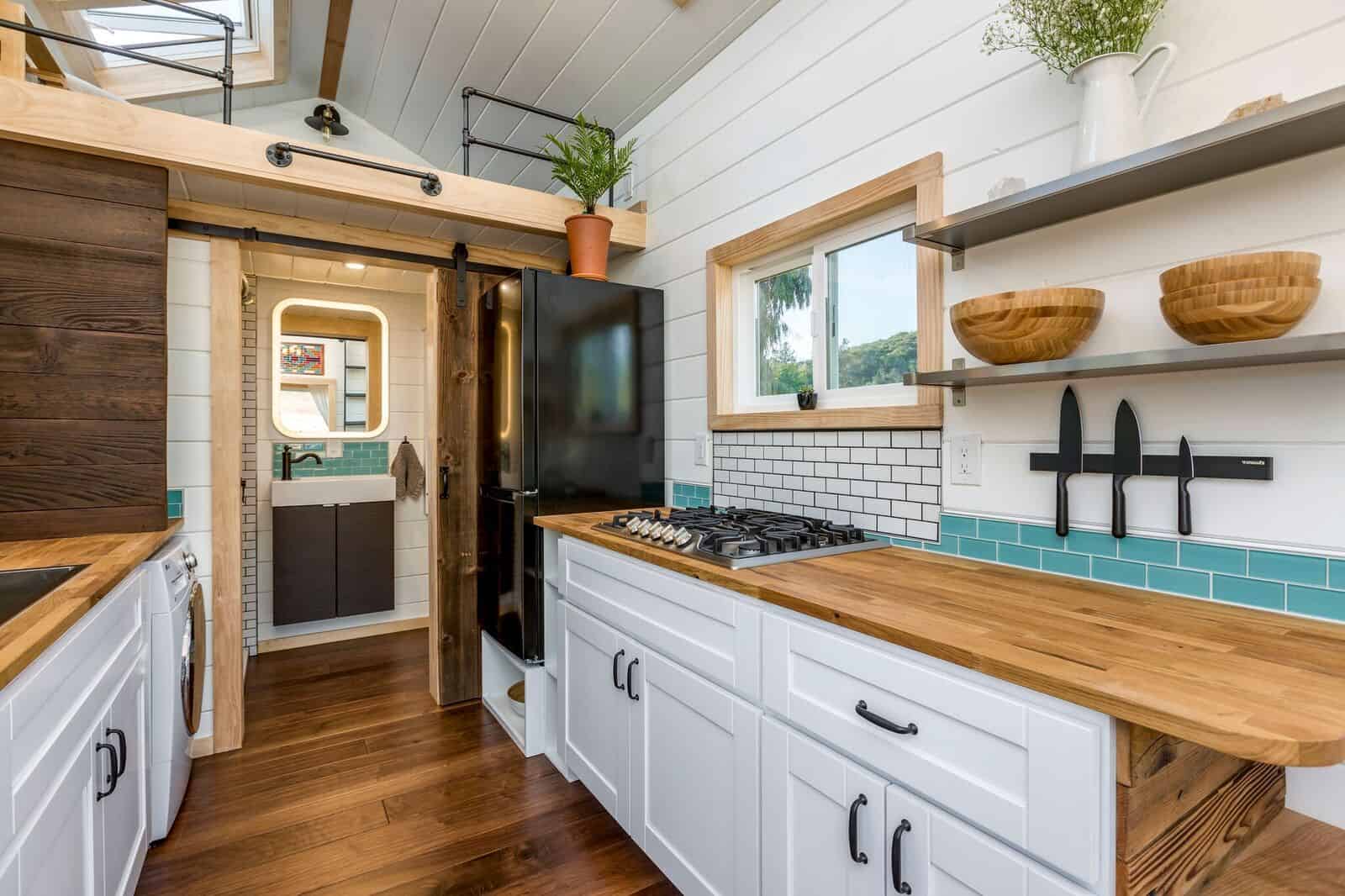 The Joshua Tree kitchen with a four-burner propane cooktop, refrigerator, and a barn-style sliding door open to the bathroom