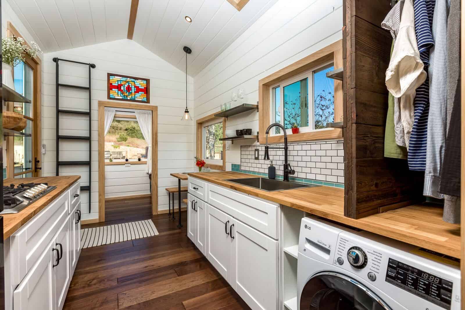 The Joshua Tree interior showing an LG washer-dryer under the counter, hanging storage, and a colorful stained-glass window over the door