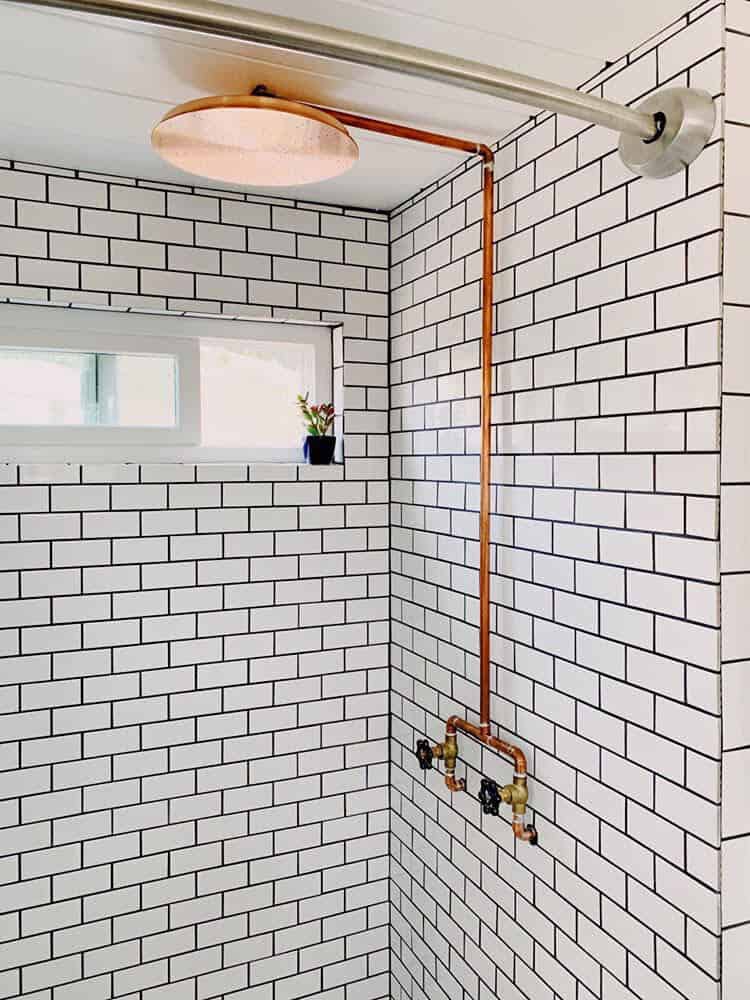 A subway-tiled shower with a custom copper rainfall shower head and exposed copper piping in the Joshua Tree tiny house