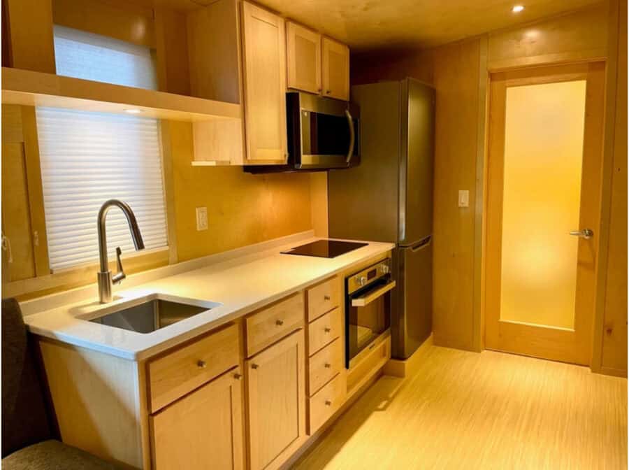 Kitchen in the Escape Boho XLS tiny house with compact appliances and wooden cabinetry.