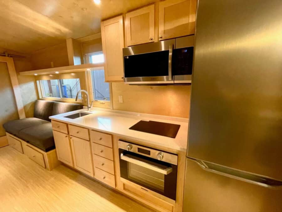 Compact tiny house kitchen featuring a sleek oven, microwave, and refrigerator. Perfect for small sp.