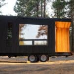 Tiny house on wheels with modern black exterior and warm wooden interior.