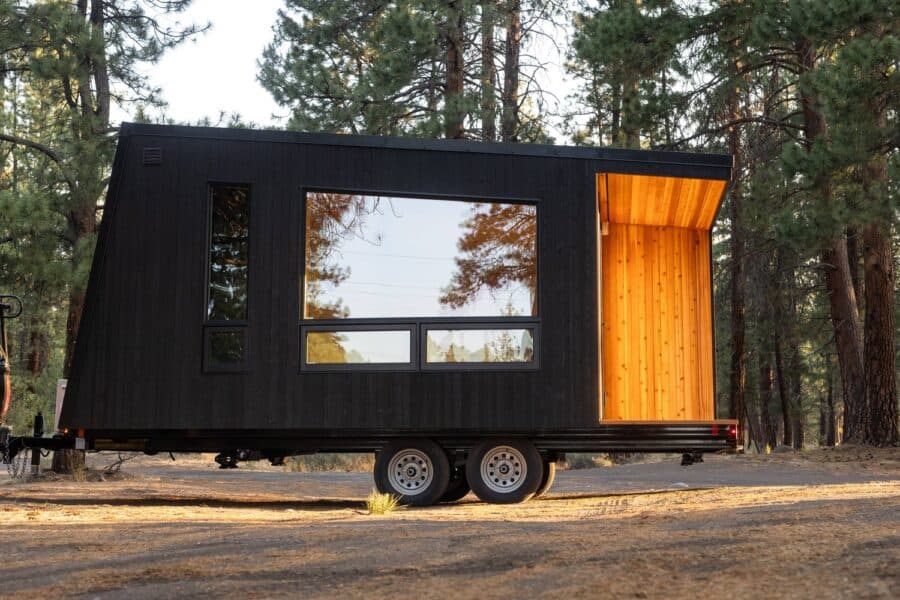 Tiny house on wheels with modern black exterior and warm wooden interior.
