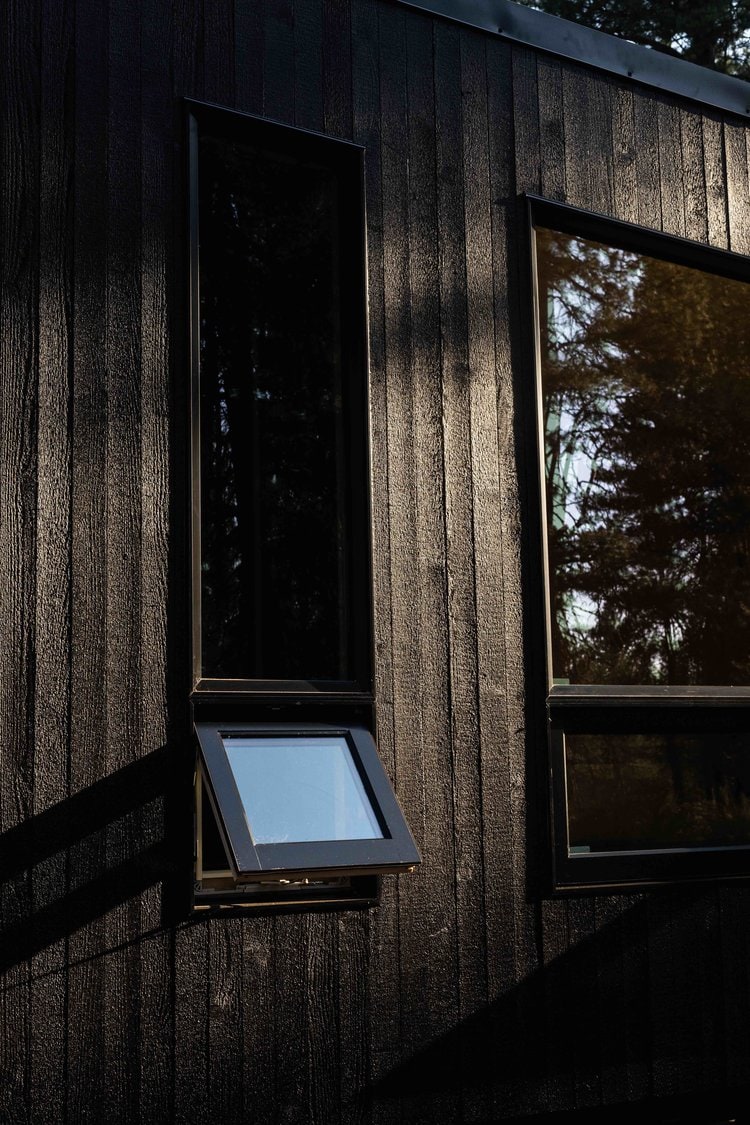 Compact tiny house with black wooden siding and large windows.