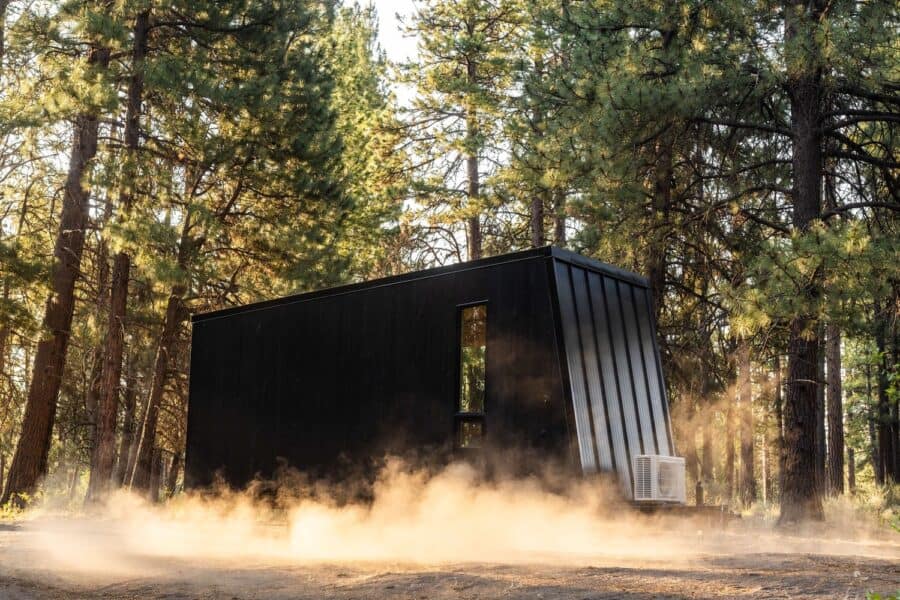 Tiny house in a forest setting with modern black exterior and minimalist design.