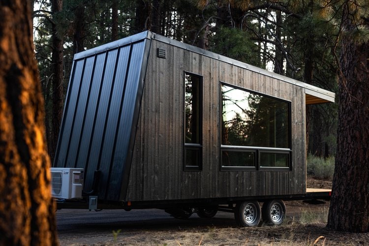 Tiny house with modern black exterior and large windows in a forest setting.