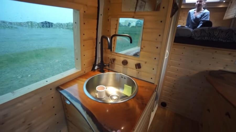 Compact tiny house van interior with a sliding bed, beautiful wood accents, and efficient storage so.