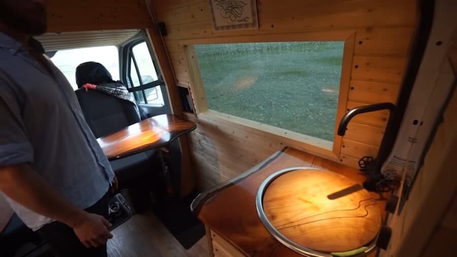 Interior of tiny house van with sliding bed and custom wood storage.
