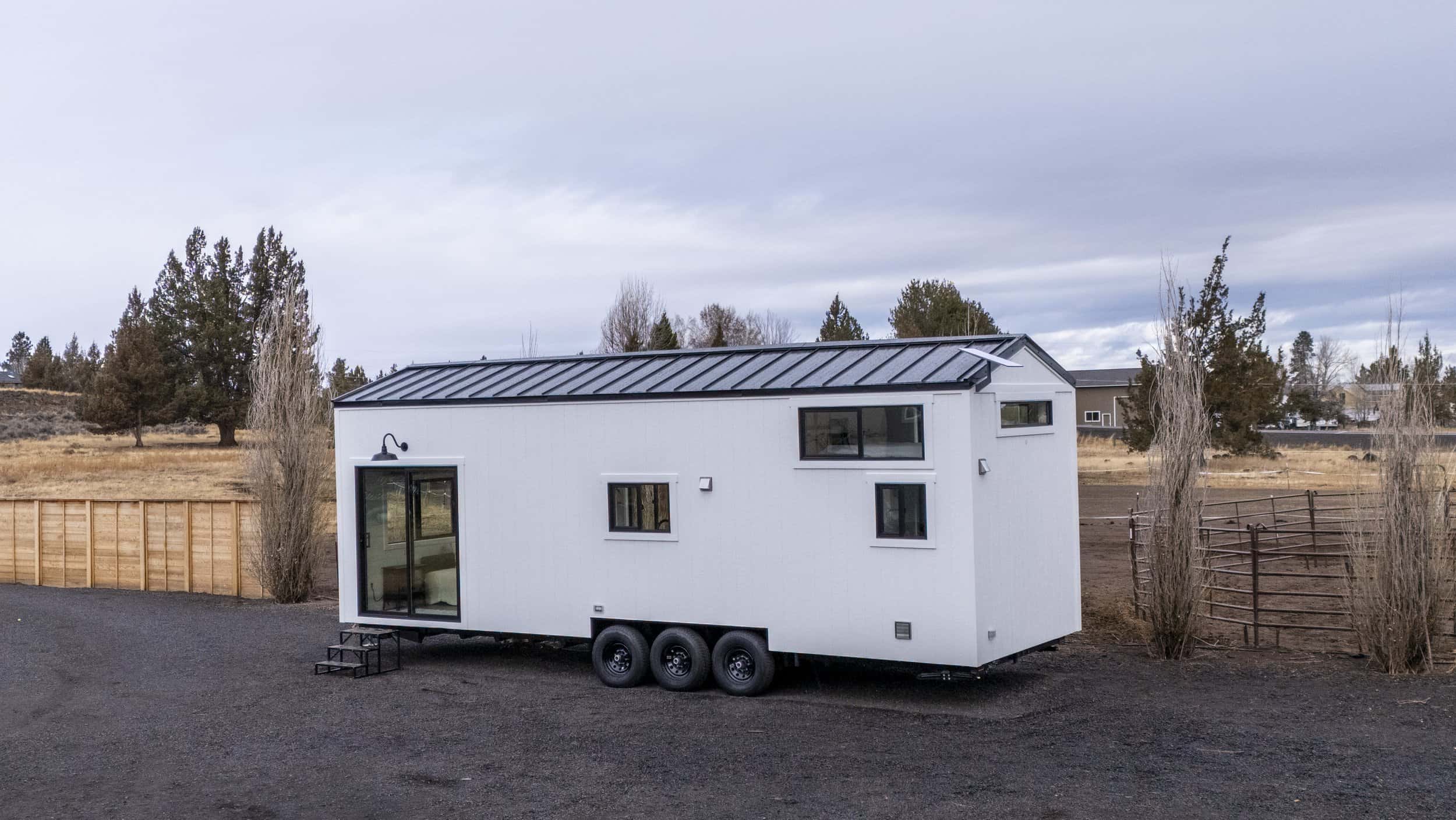 The Ochoco tiny house by Spindrift Homes with white board-and-batten siding and a black metal roof on a triple-axle trailer