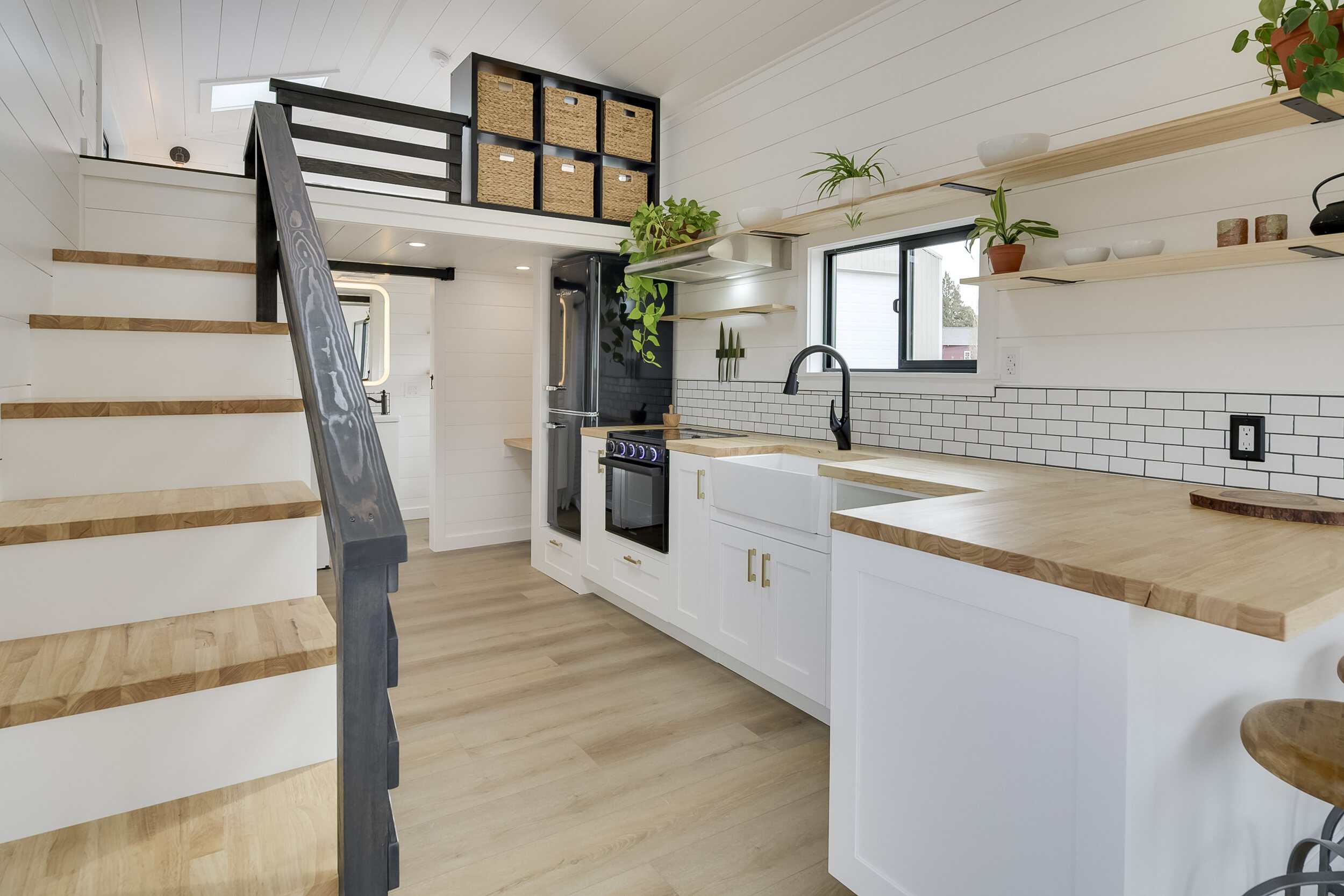 The Ochoco peninsula kitchen with butcher block counters, white cabinets, a black range, farmhouse sink, and subway tile