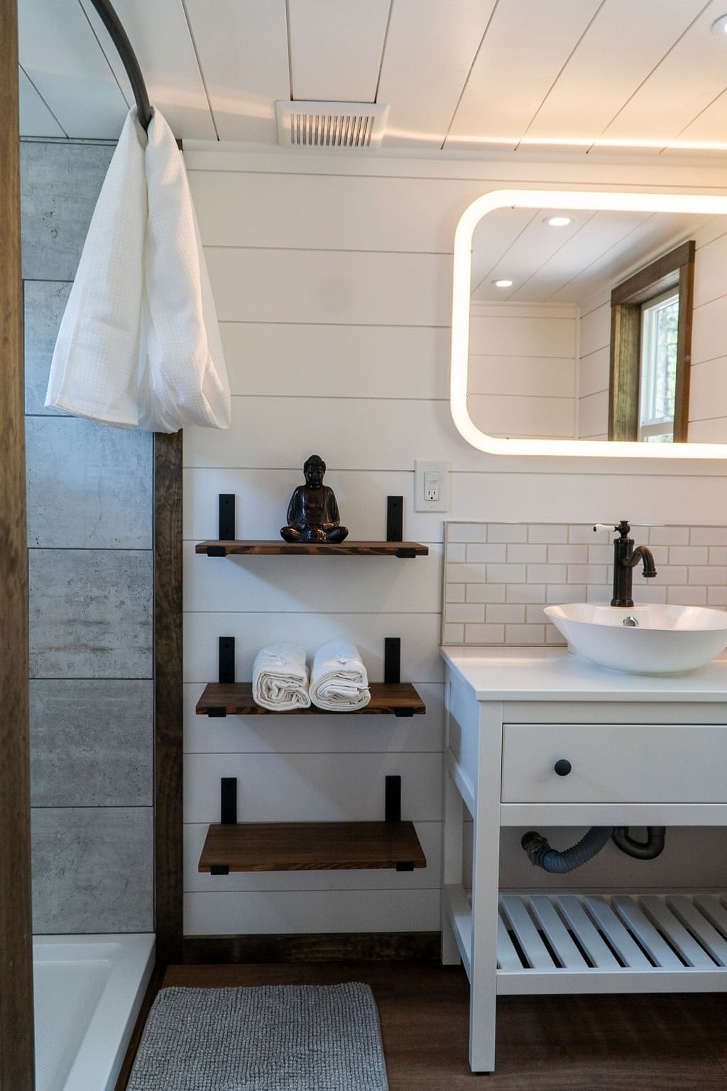The Olympic bathroom with a vessel sink, backlit mirror, floating wood shelves, and a tiled shower