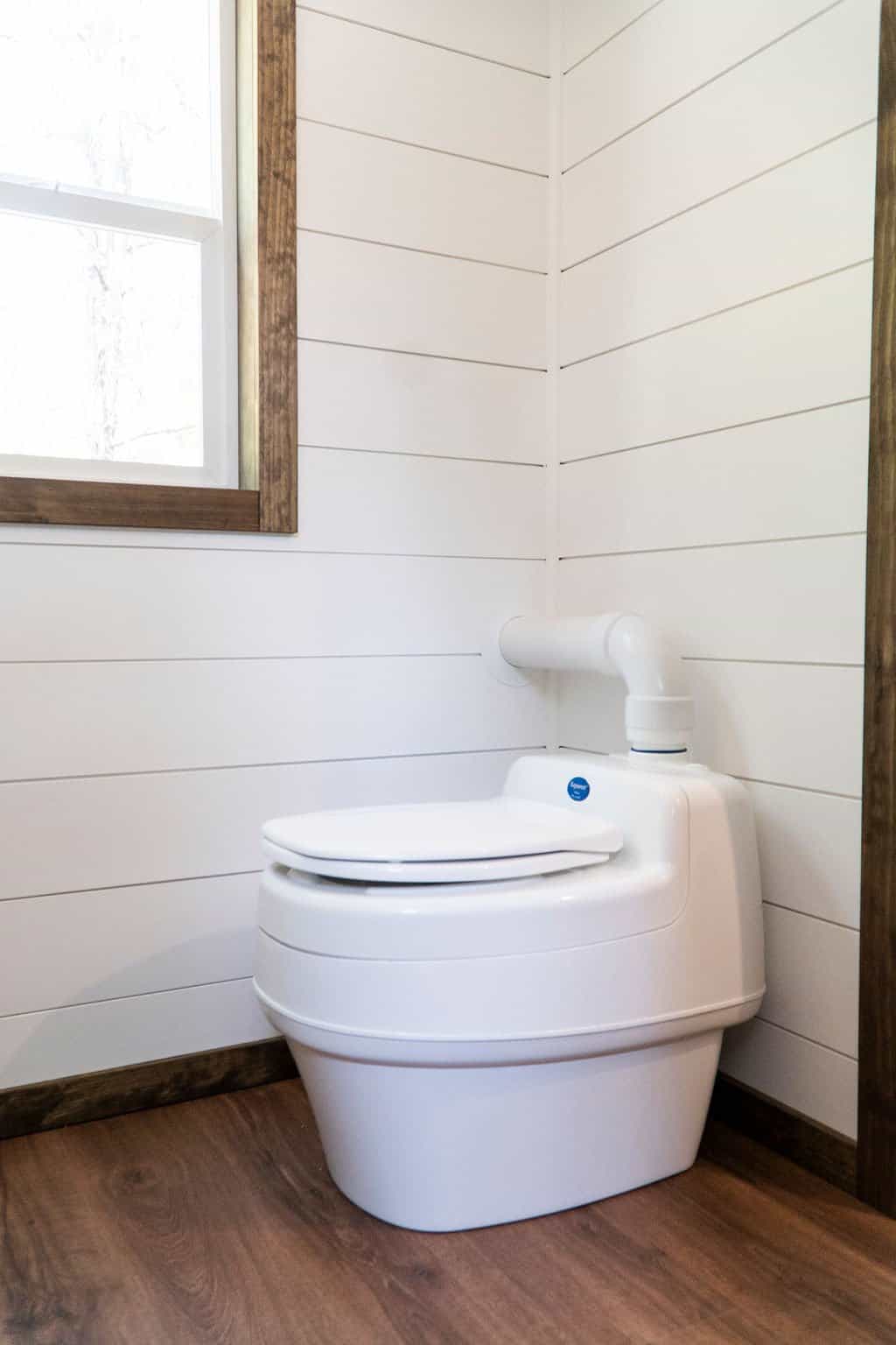 A white composting toilet against white shiplap walls in the Olympic tiny house bathroom