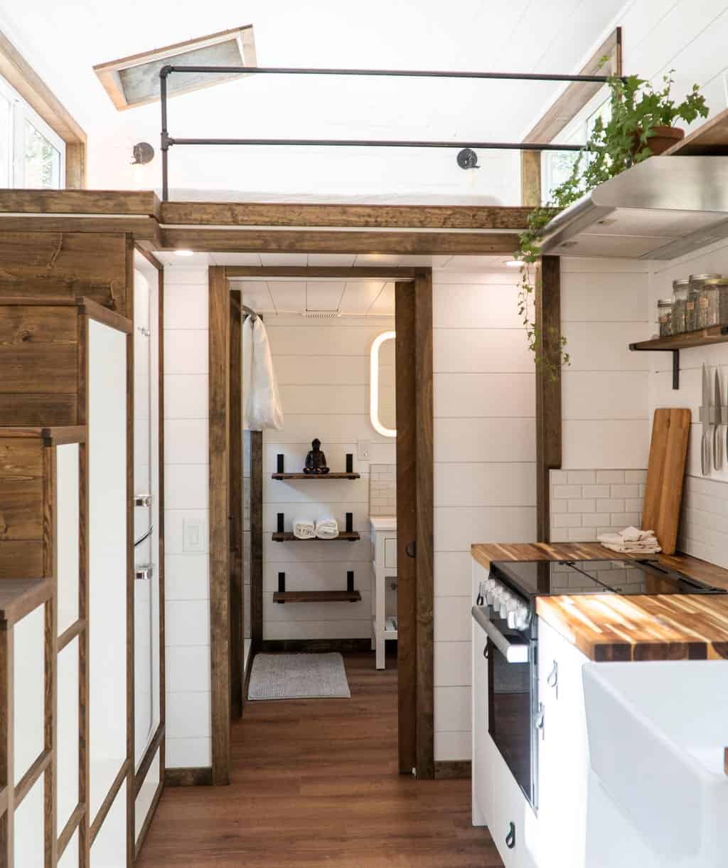 View past the Olympic's storage staircase and gas range into the bathroom with a backlit mirror and floating shelves
