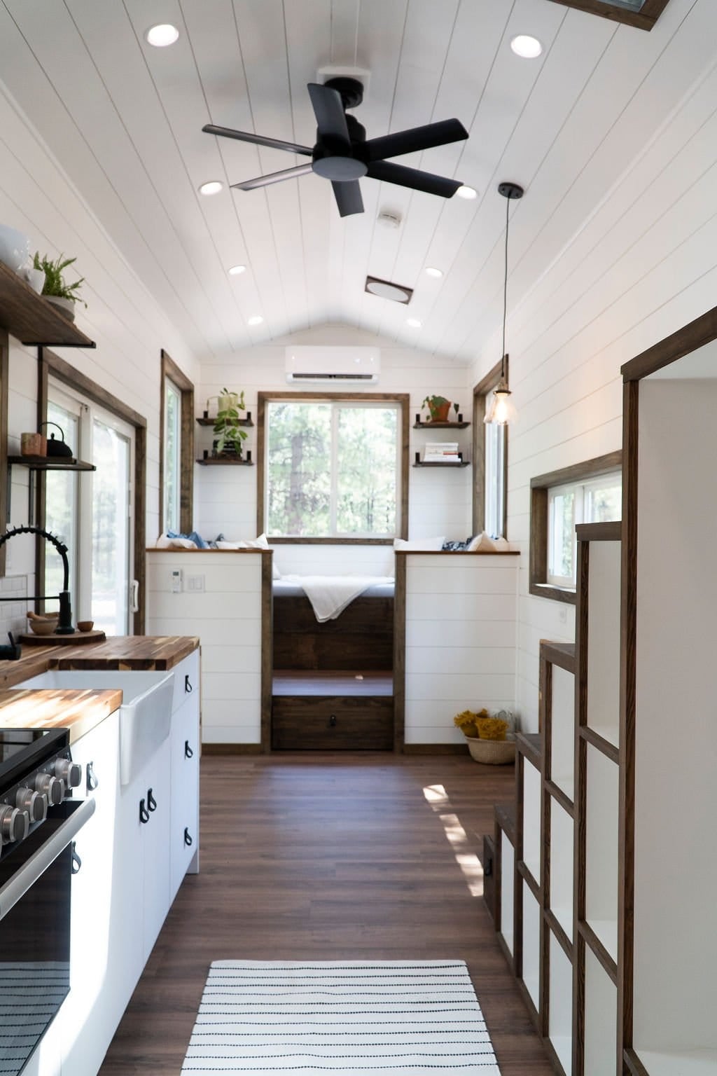 The Olympic tiny house interior showing the galley kitchen, vaulted ceiling, storage staircase, and a sunken rear lounge