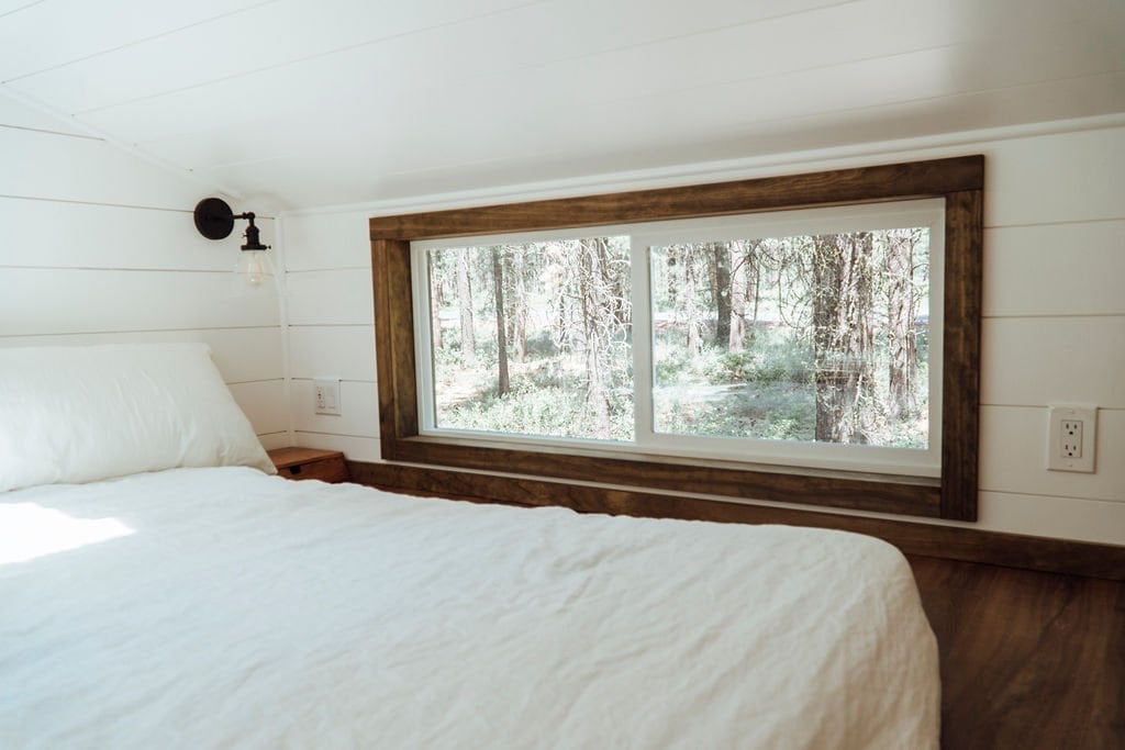 The Olympic loft bedroom with a bed and a large wood-framed window looking out into the forest