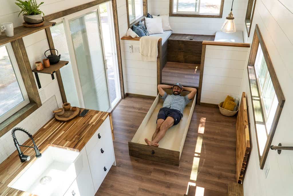 A person lying in the Olympic's full-size pull-out drawer bed built into the floor near the lounge